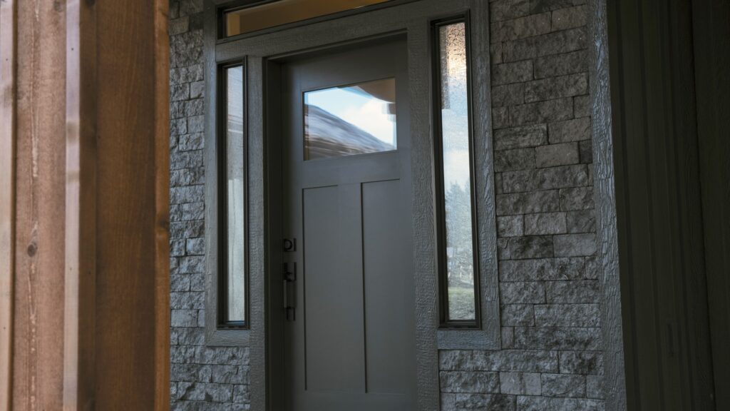 Alpenglow Builders LLC - A high-end custom home entrance with a modern gray door, flanked by stone and wood accents, in Palmer and Wasilla, Alaska.