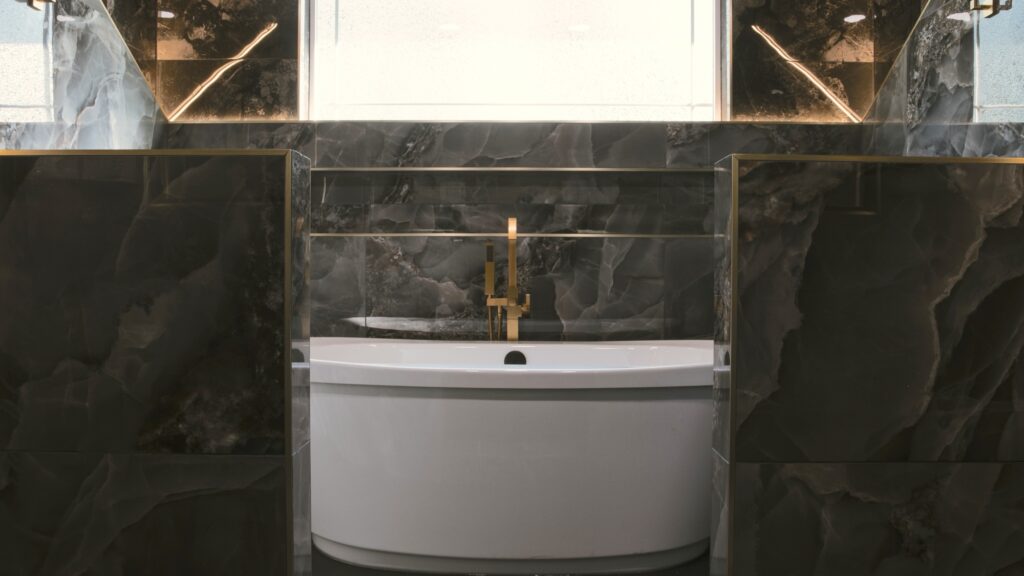 Alpenglow Builders LLC - A high-end luxury bathroom with a freestanding bathtub, black marble walls, and gold fixtures, showcasing custom design by Al.