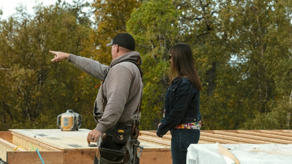 Alpenglow Builders LLC - A high-end custom luxury home under construction in Palmer, Alaska, with two professionals discussing the project amidst autu.